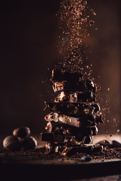 closeup view of nutmegs and grated chocolate falling on stack of chocolate pieces on wooden table - Photo, Image