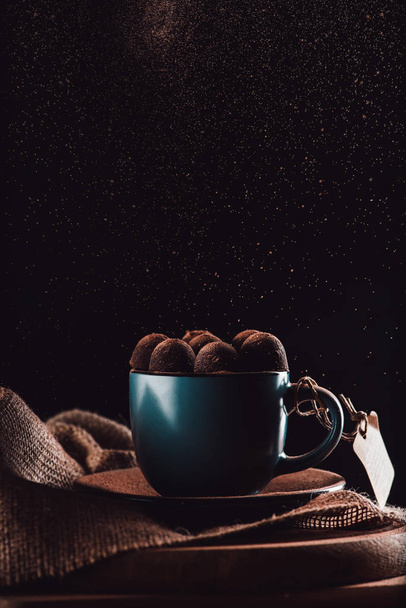 close up view of truffles in cup of coffee on sackcloth and cutting board on black background  - Fotó, kép