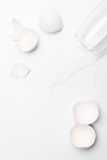 bovenaanzicht van gebroken kip eierschalen met gemorste melk op witte ondergrond - Foto, afbeelding