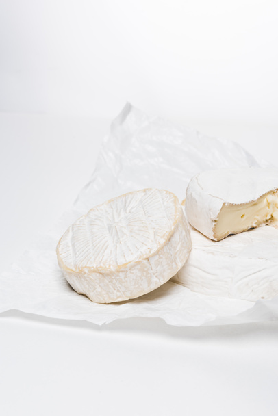 lähikuva maukasta brie-juustoa rypistyneellä paperilla ja valkoisella pinnalla
 - Valokuva, kuva