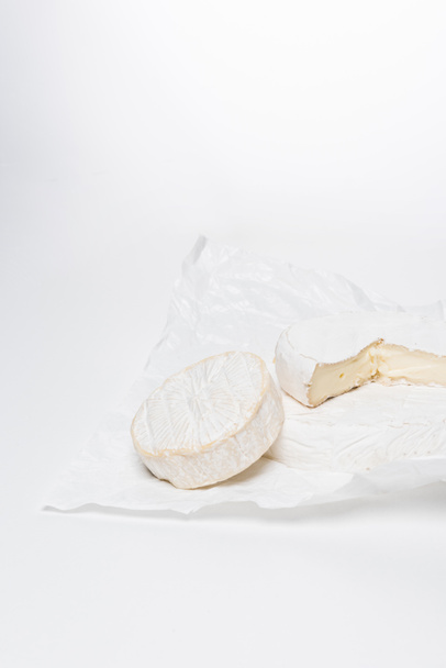 close-up shot of brie cheese on crumpled paper and on white surface - Foto, Bild