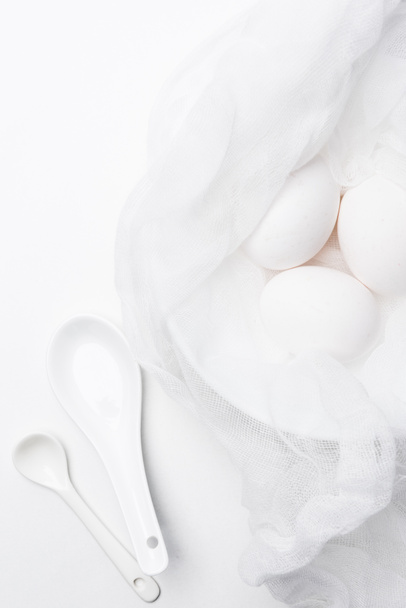 top view of raw chicken eggs in cheesecloth with spoons on white surface - Fotoğraf, Görsel