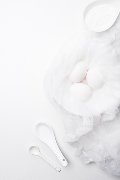 vista dall'alto di uova di pollo crude in garza con panna acida in cucchiaio su superficie bianca
 - Foto, immagini