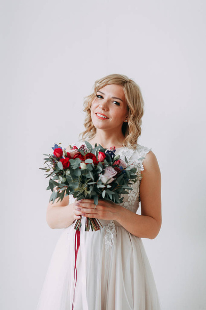 Beautiful bride in a wedding dress in a bright stylish Studio. Wedding in European style. Decor and bouquet in hand. Young girl standing, sitting and posing - Photo, Image