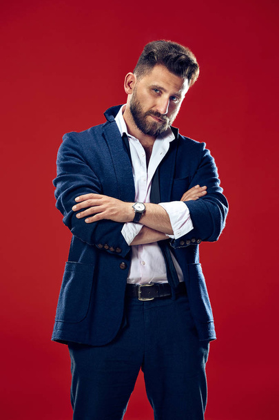 Male beauty concept. Portrait of a fashionable young man with stylish haircut wearing trendy suit posing over red background. - Foto, immagini