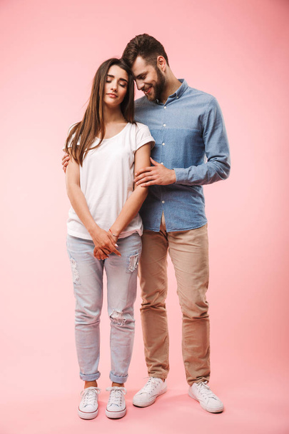 Ganzkörperporträt eines schönen jungen Paares, das sich umarmt, während es isoliert auf rosa Hintergrund steht - Foto, Bild