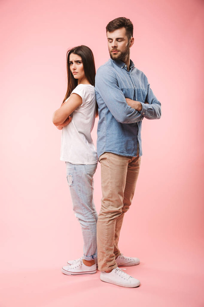 Full length portrait of an angry young couple standing back to back isolated over pink background - Foto, Imagem