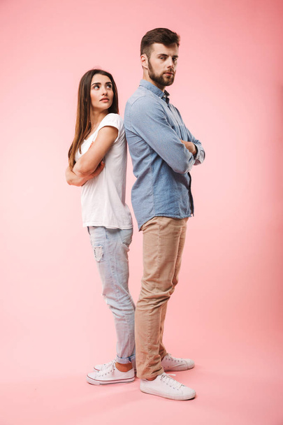 Full length portrait of a disappointed young couple standing back to back isolated over pink background - Fotó, kép
