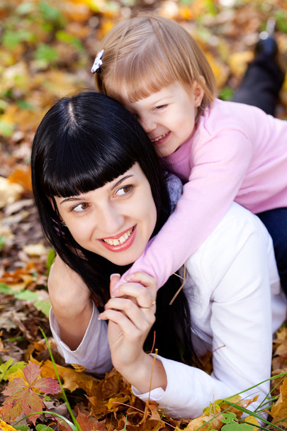 beautiful young mother and her daughter lying on the autumn leav - Photo, image