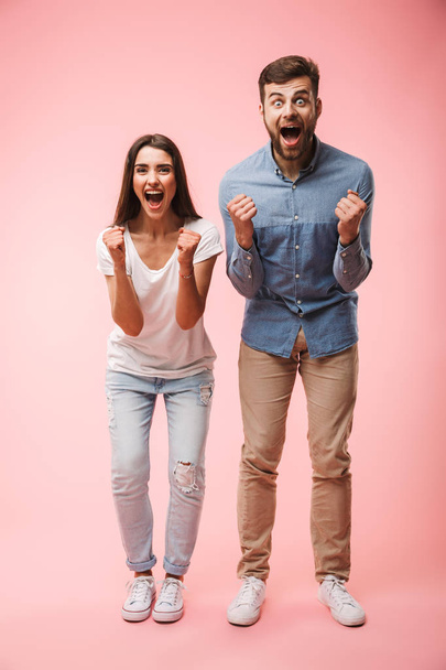 Full length portrait of an excited young couple screaming and looking at camera isolated over pink background - Foto, Bild