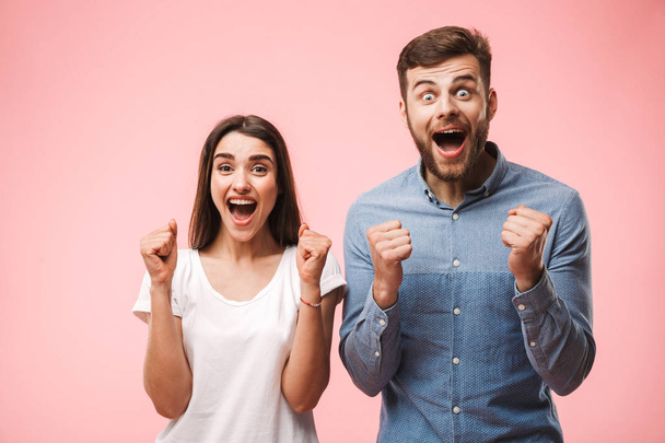 Portrait of an excited young couple screaming and looking at camera isolated over pink background - Fotoğraf, Görsel