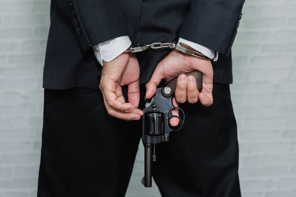 Arrested businessman in handcuffs and hold gun with hands behind back - Foto, Imagem