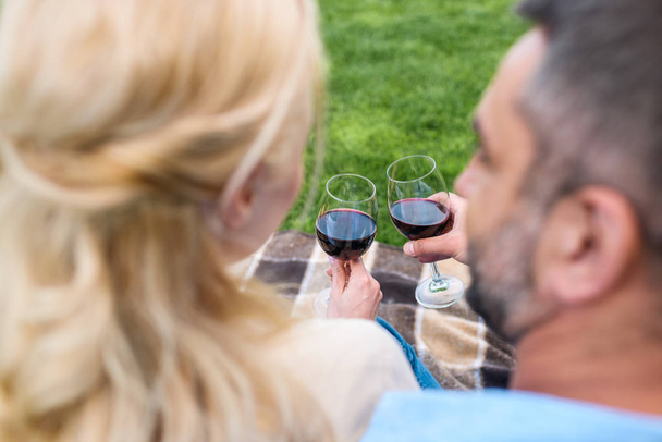 selective focus of couple holding glasses of wine while sitting together at picnic - Photo, image