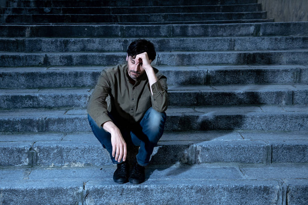 latin man stressed from work sitting on steps outside feeling anxiety in adult cause of depression and problem in living that makes you feel lonely, sad and worried in mental health concept - Фото, изображение