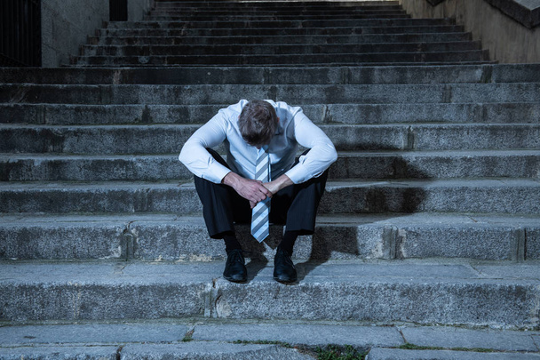 young business man crying abandoned lost in depression sitting on the street stairs suffering emotional pain, sadness in a mental health concept photo - Photo, Image