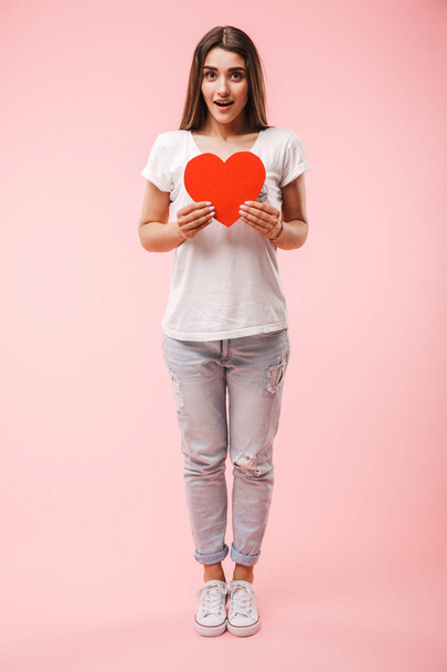 Full length of a pretty young woman holding red heart isolated over pink background - Фото, зображення