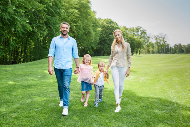happy family holding hands and smiling at camera while walking together in park - Foto, imagen