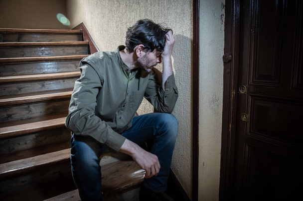 depressed latin man sitting head in hands inside in a stairwell feeling lonely and sad and stressed about work and life in a mental health concept - Fotó, kép