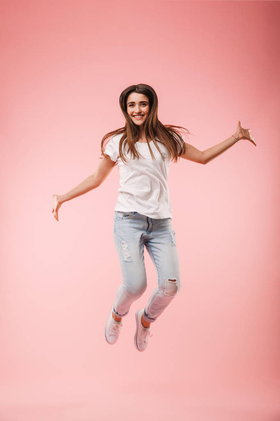 Full length of an excited young woman jumping isolated over pink background - Φωτογραφία, εικόνα