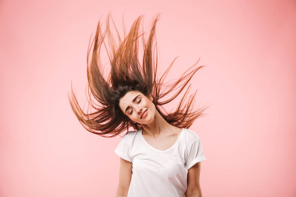 Portrait of a smiling young woman with long hair jumping isolated over pink background - Fotoğraf, Görsel