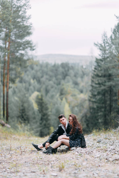 Young stylish couple in the forest, running around the Park and laughing. Modern people on a walk. Beautiful girl with tattoos. Loving young man and girl. mountain Park with pine forest - Photo, image