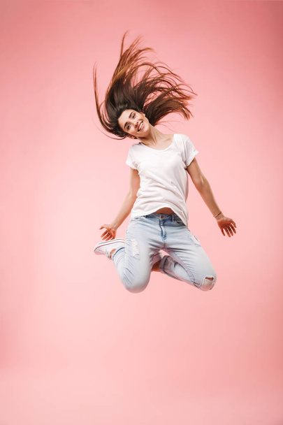 Full length of an excited young woman with long hair jumping isolated over pink background - Фото, изображение