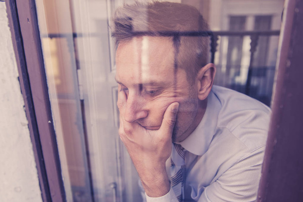 Close up portrait of middle aged man sad and depressed looking through the window refection, thinking about his life suffering depression in mental health concept - Zdjęcie, obraz