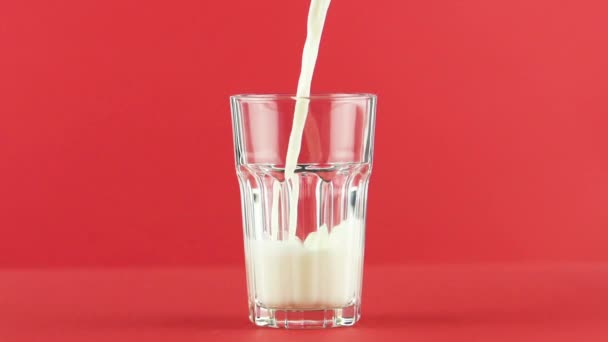 Slow motion close-up shot van koude dagboek melk koud drankje drinken massasprint in in facetgeslepen glas op gekleurde rode achtergrond in de studio - Video