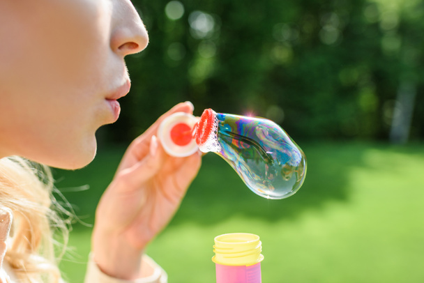обрізаний знімок молодої жінки, що дме мильні бульбашки в парку
 - Фото, зображення