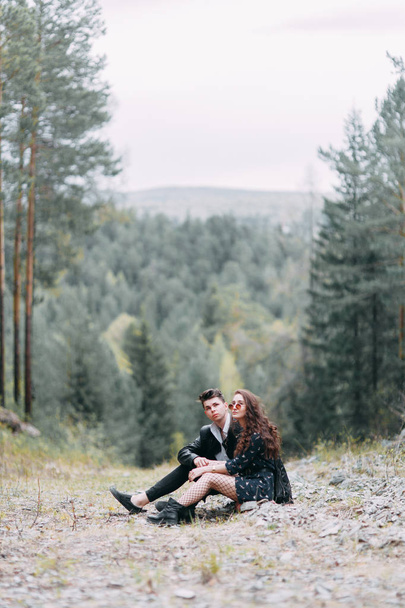 Young stylish couple in the forest, running around the Park and laughing. Modern people on a walk. Beautiful girl with tattoos. Loving young man and girl. mountain Park with pine forest - Foto, Imagem