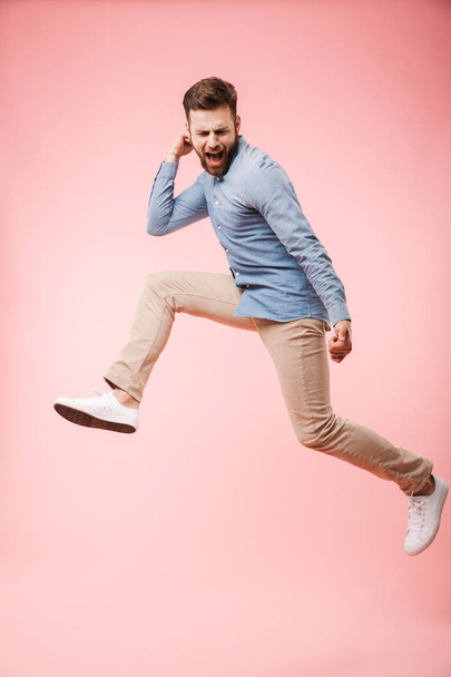 Full length of an excited young man jumping and celebrating success isolated over pink background - Valokuva, kuva