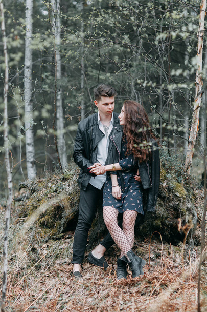 Young stylish couple in the forest, running around the Park and laughing. Modern people on a walk. Beautiful girl with tattoos. Loving young man and girl. mountain Park with pine forest - Fotó, kép