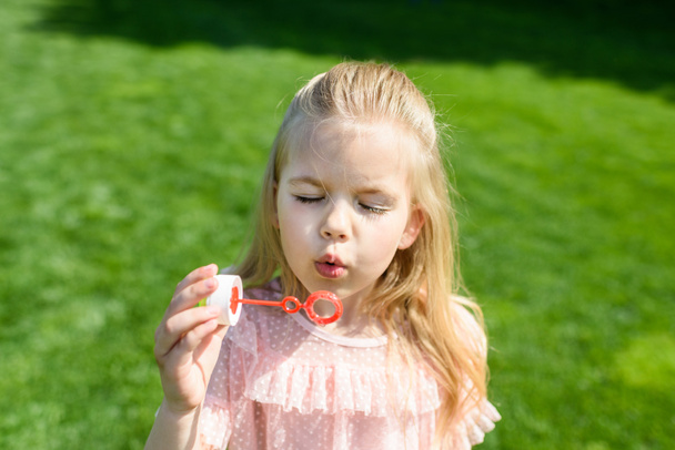 adorable little child blowing soap bubbles in park - Foto, afbeelding