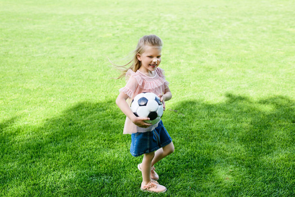 μεγάλη γωνία προβολής ευτυχισμένη μικρού παιδιού, κρατώντας την μπάλα ποδοσφαίρου στο γρασίδι - Φωτογραφία, εικόνα