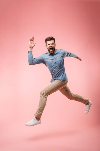 Full length of a cheerful young man running and celebrating success isolated over pink background - Foto, Imagen