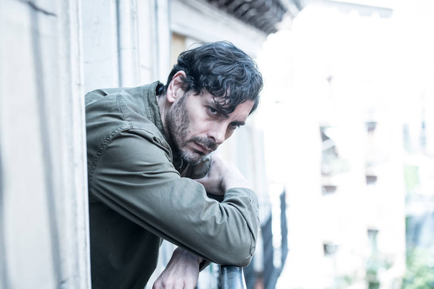close up portrait of sad and depressed man looking out the window on a balcony at home suffering depression and felling lonely in mental health concept - 写真・画像