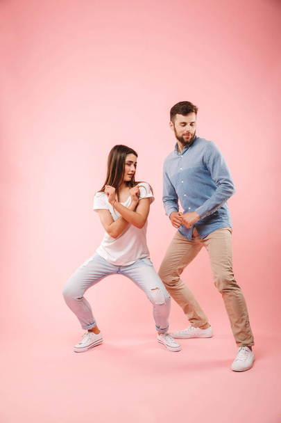 Full length portrait of a happy young couple dancing together isolated over pink background - Foto, Imagen
