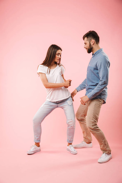 Full length portrait of a cheerful young couple dancing together isolated over pink background - Foto, immagini