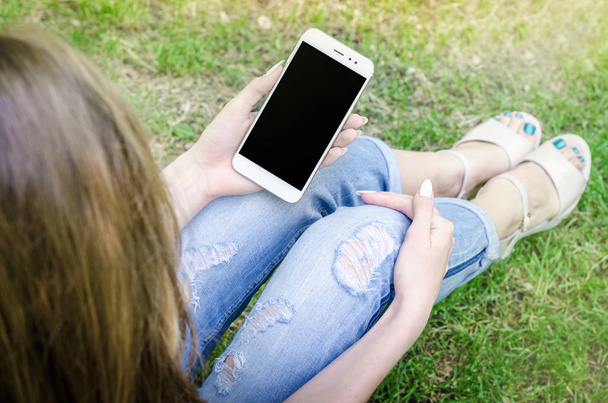 Lähikuva valkoinen älypuhelin Mobile Cell tilalla naisen käsissä Tyylikäs revitty Farkut Pitkät kynnet Denim Musta Oled Näyttö Luonto Tausta
 - Valokuva, kuva