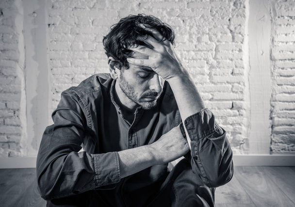 young depressed man sitting against a white wall at home with a shadow on the wall feeling miserable, lonely and sad in mental health depression concept - Photo, image