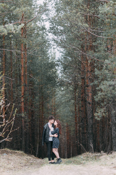 Young stylish couple in the forest, running around the Park and laughing. Modern people on a walk. Beautiful girl with tattoos. Loving young man and girl. mountain Park with pine forest - Foto, Bild