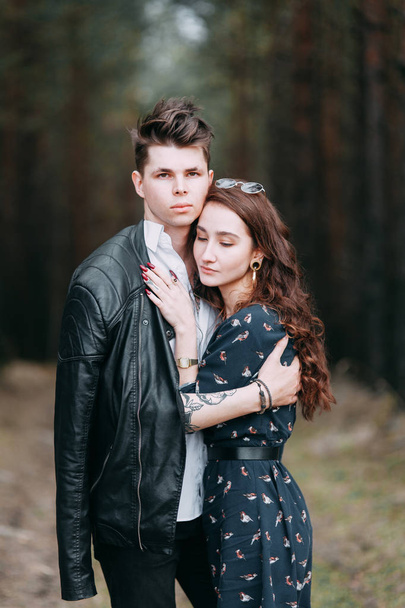 Young stylish couple in the forest, running around the Park and laughing. Modern people on a walk. Beautiful girl with tattoos. Loving young man and girl. mountain Park with pine forest - Fotografie, Obrázek