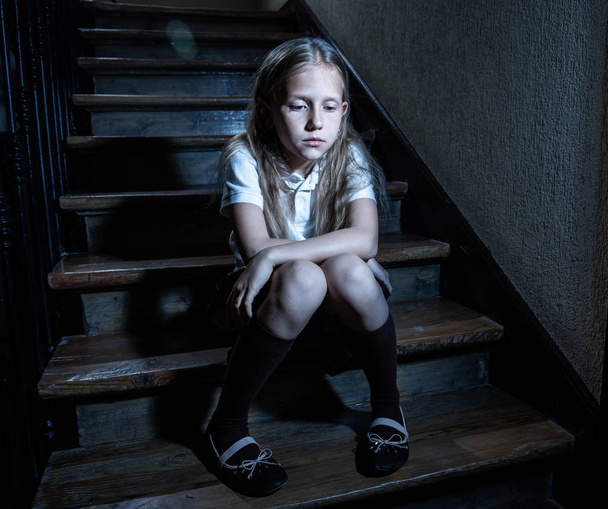 Sad, depressed, unhappy schoolgirl suffering from bullying and abuse feeling lonely and hopeless sitting on stairs with dark light. School isolation, bullying, harassment and abuse concept - Zdjęcie, obraz