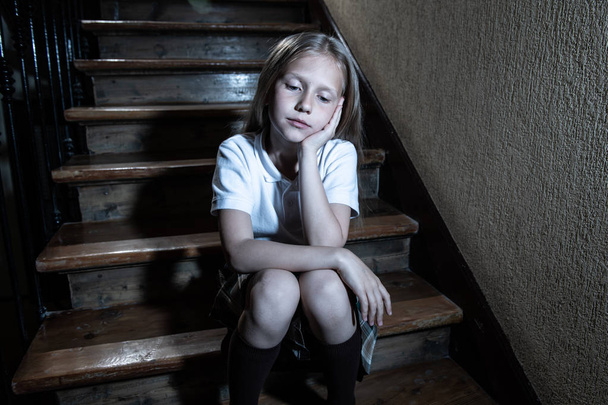 Sad, depressed, unhappy schoolgirl suffering from bullying and abuse feeling lonely and hopeless sitting on stairs with dark light. School isolation, bullying, harassment and abuse concept - 写真・画像