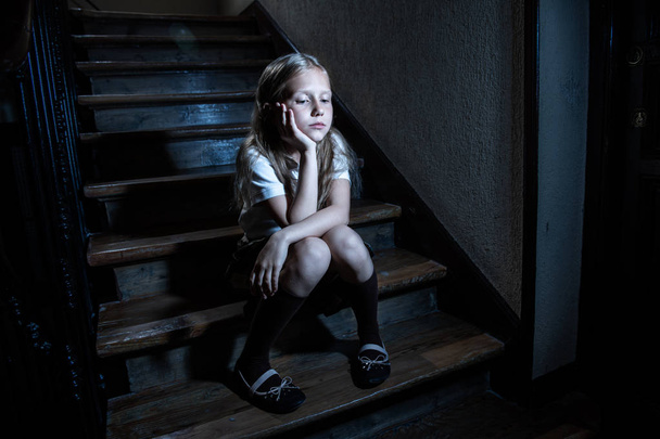 Sad, depressed, unhappy schoolgirl suffering from bullying and abuse feeling lonely and hopeless sitting on stairs with dark light. School isolation, bullying, harassment and abuse concept - Valokuva, kuva