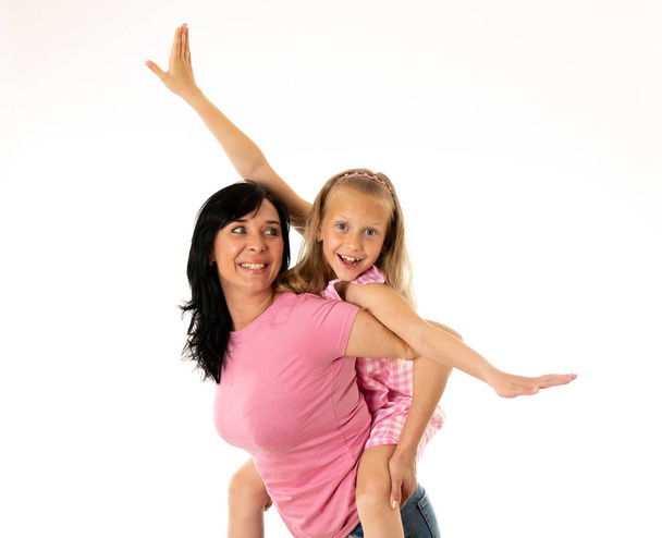 Portrait of a happy mother and cute blonde little girl hugging and looking cheerful at the camera in studio on white background. Happy family and good and positive parent and child relationship - Foto, imagen