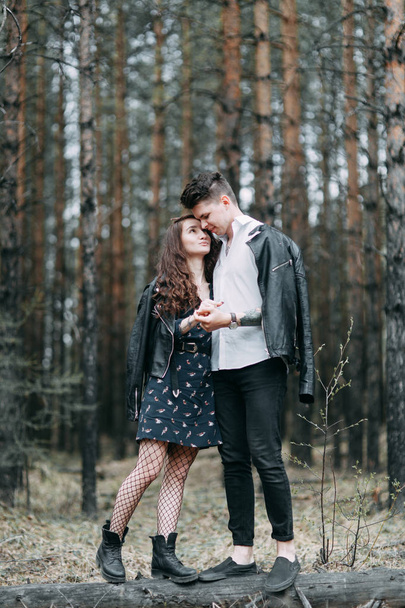 Young stylish couple in the forest, running around the Park and laughing. Modern people on a walk. Beautiful girl with tattoos. Loving young man and girl. mountain Park with pine forest - Foto, Bild