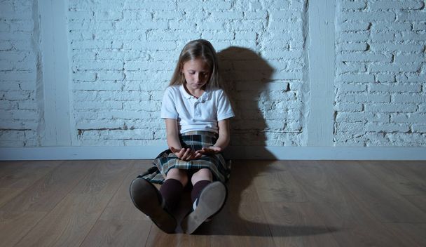 Sad desperate young girl suffering from bulling and harassment felling lonely, unhappy desperate and hopeless sitting against the wall, dark light. School isolation, abuse and bullying concept - Фото, зображення