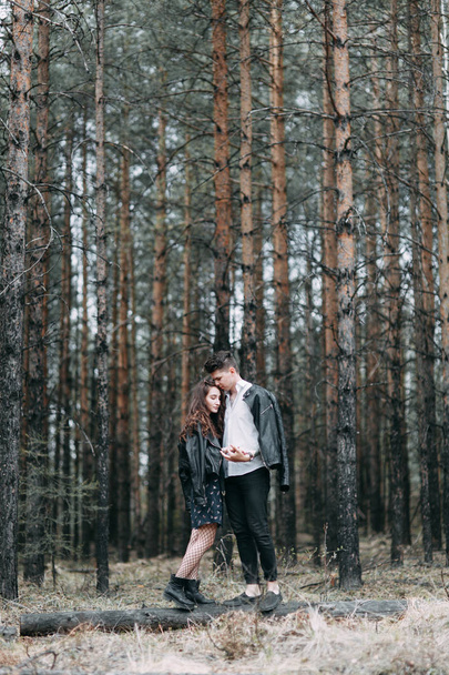 Young stylish couple in the forest, running around the Park and laughing. Modern people on a walk. Beautiful girl with tattoos. Loving young man and girl. mountain Park with pine forest - Valokuva, kuva