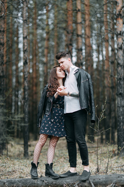 Young stylish couple in the forest, running around the Park and laughing. Modern people on a walk. Beautiful girl with tattoos. Loving young man and girl. mountain Park with pine forest - Zdjęcie, obraz